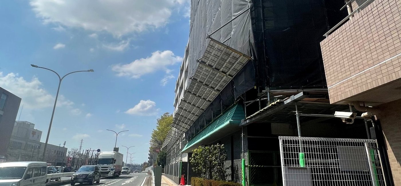 道路沿いの建物に架けた足場と飛散防止ネット、歩行者を守る防護棚